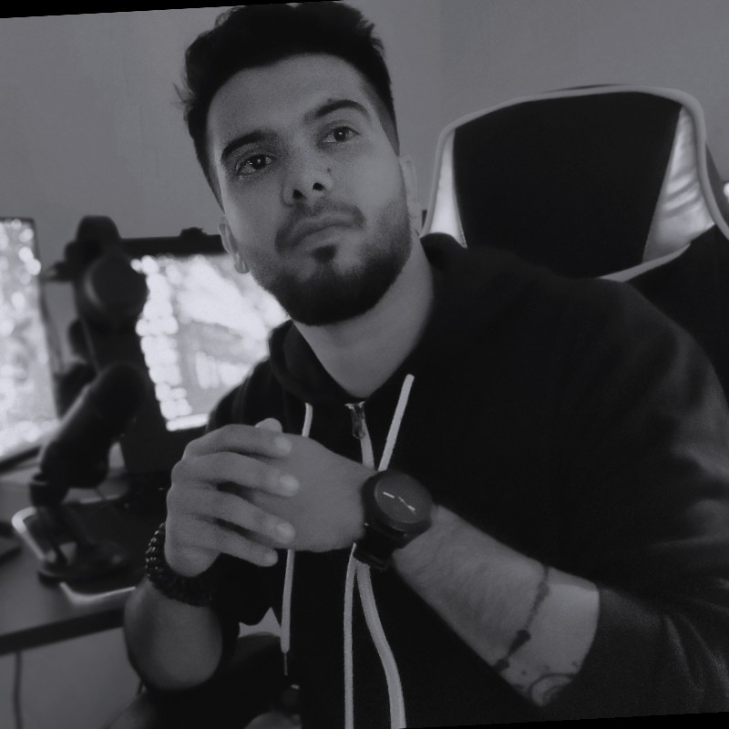 Black and white photo of Vinod Krishnan sitting in a van. The camera is angled so the picture is artistically off-balance. Vinod is a young man with dark hair and what would be golden brown or olive skin if the picture were not in black and white. in the picture. His gaze is lookin off toward the viewers right and he sports a mustache and short beard.