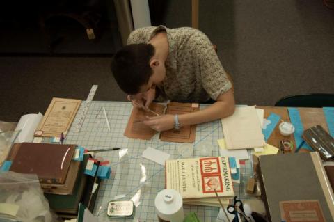 Student worker Kathryn Higinbothom working on repairing a rare book's spine from the museum's collection